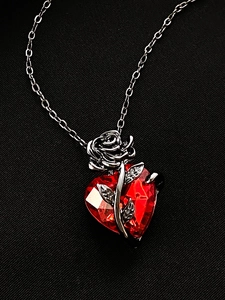 Detail of red heart zircon necklace with silver rose decoration on black background