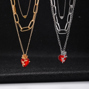 Detail of layered gold and silver necklace featuring a red heart crystal and rose relief