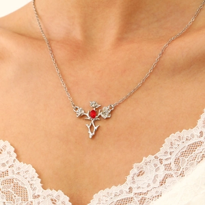 Detail view of silver necklace with red oval gemstone and carved roses on lace dress