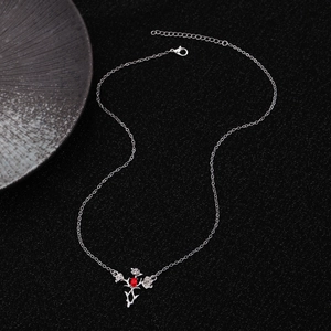 Detailed view of silver rose pendant necklace with vibrant red oval gemstone on black surface