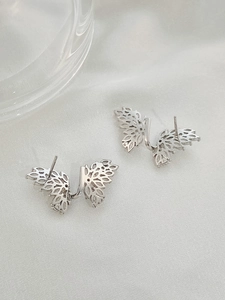 Detail of silver hollow butterfly stud earrings with intricate wing textures on silk