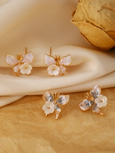 Detail of gold butterfly earrings with pink and white marble texture and floral accents