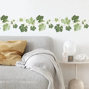 Self-adhesive green leaf vine wall stickers for living room decor above a grey sofa