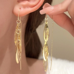 Detail of long gold leaf tassel earrings with hollow link design worn by a model