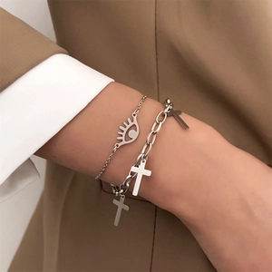 Detail of layered silver bracelets featuring evil eye charm and triple cross pendants