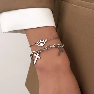 Detail of silver chain bracelet set with eye and cross charms worn with a brown blazer