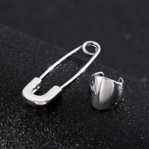 Macro shot of a silver safety pin earring and wide ear cuff on black textured background