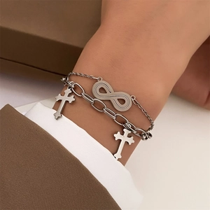 Silver infinity and cross chain bracelets layered style on model wrist with brown sleeve