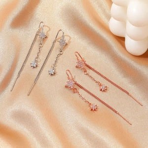 Detail view of elegant tassel leaf earrings in silver and rose gold on gold silk fabric