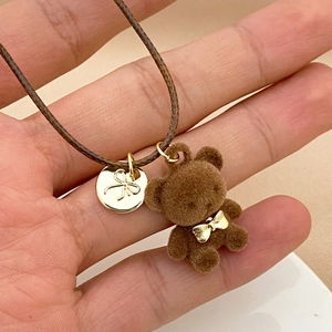 Dettaglio di un ciondolo a forma di orsetto marrone con fiocco dorato e medaglietta
