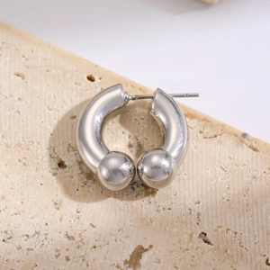 Detailed close-up of a silver horseshoe barbell earring on a textured beige stone background
