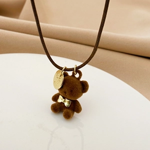 Dettaglio del ciondolo a forma di orsetto di peluche marrone con fiocco d'oro