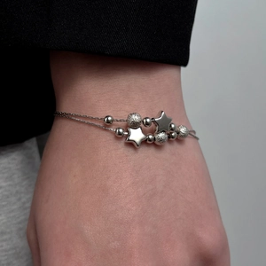 Detail of silver double-layer chain bracelet featuring star charms and frosted beads