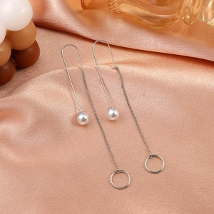 Detail of silver tassel chain earrings with white pearl and hollow ring on silk fabric