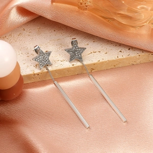 Detail of silver tassel earrings with star zircon studs on light pink silk fabric