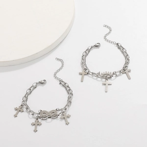 Detail of silver double-layer cross bracelet with infinity and sun charms on white base