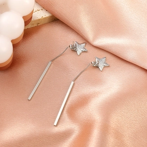 Detail view of silver tassel earrings with star studs on elegant silk and marble background