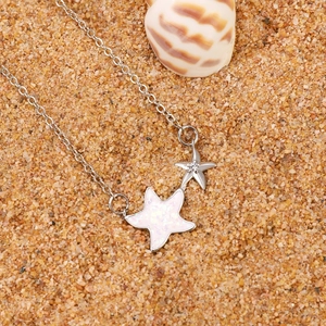 Minimalist silver starfish pendant necklace with opal inlay on sandy beach background