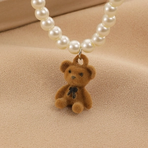 Macro del ciondolo a forma di orsetto marrone peluche e collana di perle su tessuto