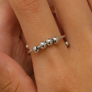 Macro detail of fidget anxiety ring with five rotating silver beads on a finger