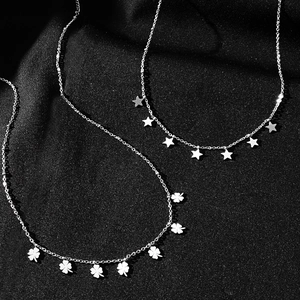 Detail of silver titanium steel necklaces with star and clover charms on black fabric