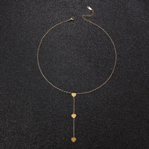 Detail of gold-plated Y-necklace featuring three heart pendants on a black surface