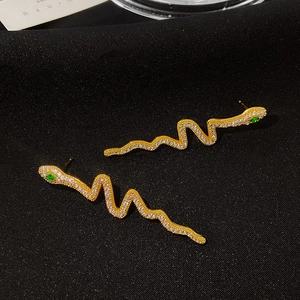 Nahaufnahme goldener Schlangenohrringe mit Zirkonia und grünen Kristallaugen auf schwarzem Stoff
