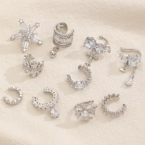 Set di earcuff e orecchini argentati con zirconi brillanti su sfondo in tessuto di lino