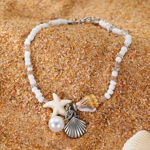 Detail of beach anklet with starfish, shell, and pearl charms on a fine sand background