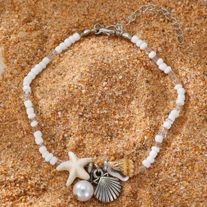 Bohemian beach anklet with starfish and shell charms on white beads over sand