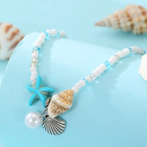 Detailed close-up of starfish, shell and pearl charms on a blue beaded beach anklet