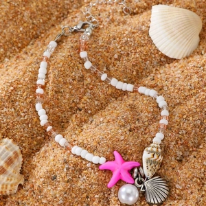 Detail view of starfish, seashell and pearl charms on a bohemian beaded beach anklet