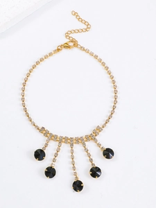 Détail d'un collier à franges doré avec pendentifs noirs et strass brillants sur fond blanc