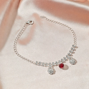 Détail d'une chevillère argentée avec gemme rouge et pampilles en strass brillant sur satin