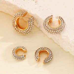 Dettaglio macro di quattro ear cuff dorati a forma di C con strass trasparenti brillanti