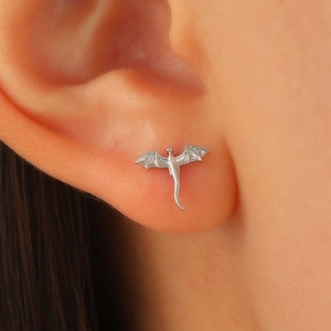 Close-up of a silver dragon stud earring with detailed wings on a woman's ear