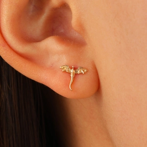 Macro shot of a tiny gold dragon stud earring worn on ear featuring detailed wings and tail