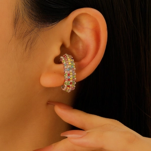 Dettaglio di ear cuff a forma di C con strass colorati e perle bianche sull'orecchio