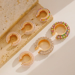 Dettaglio di ear cuff a C con strass colorati e perle su base di marmo beige