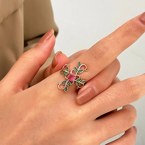 Close-up of rose gold ring with pink gemstone and green enamel leaves on hand