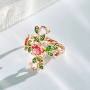 Macro shot of rose gold ring featuring pink stone, green enamel leaves and red gems