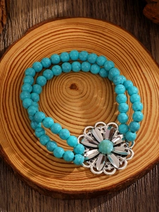 Detail of bohemian turquoise beaded bracelet with silver floral charm on wooden slice