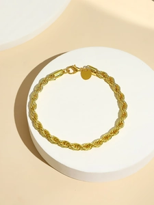 Detail of a gold rope chain bracelet featuring a lobster clasp and round polished tag