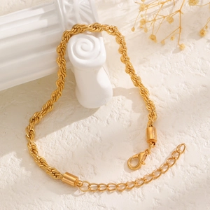 Detailed view of golden rope chain bracelet with lobster clasp on a white textured background