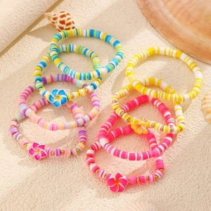 Detalle de pulseras de arcilla polimérica con flores de plumeria sobre la arena