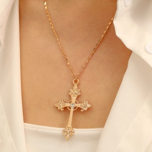 Close-up of gold plated cross necklace featuring colorful crystals on a white shirt
