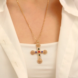 Close-up of gold cross pendant with colorful gemstones on a white shirt