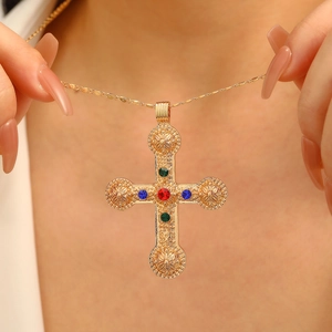 Close-up of gold cross pendant with colorful gemstones worn on a female model