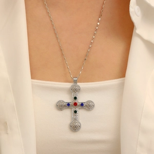 Detail of silver cross pendant with colorful gemstones worn on a white shirt
