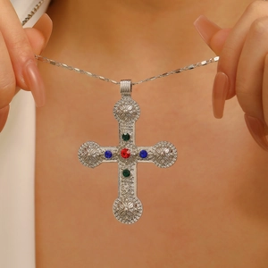 Close-up of vintage silver cross pendant with colorful gemstones held by hands